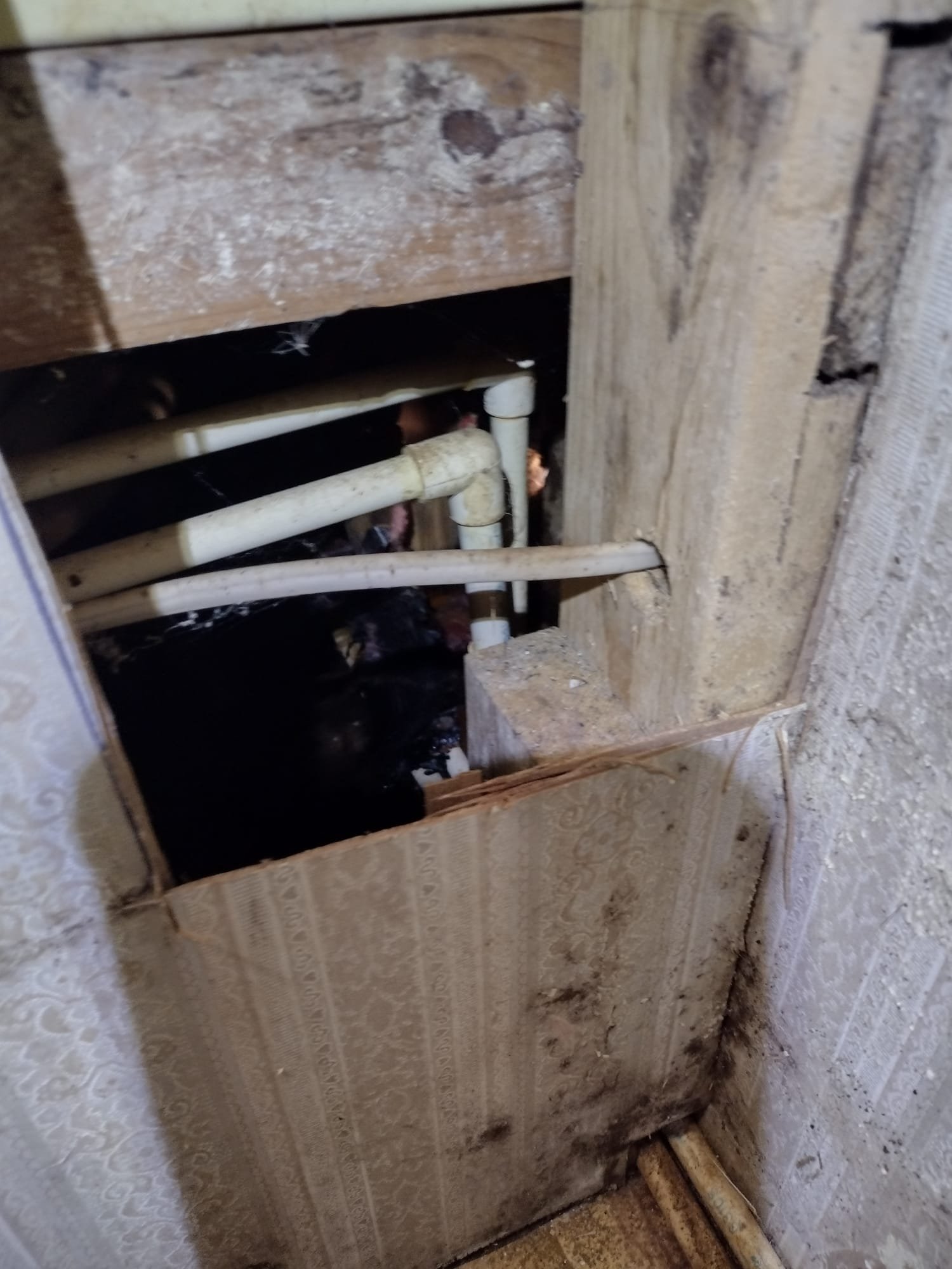 Image showing an aged plumbing setup before repair, with an opening in the wall revealing worn pipes