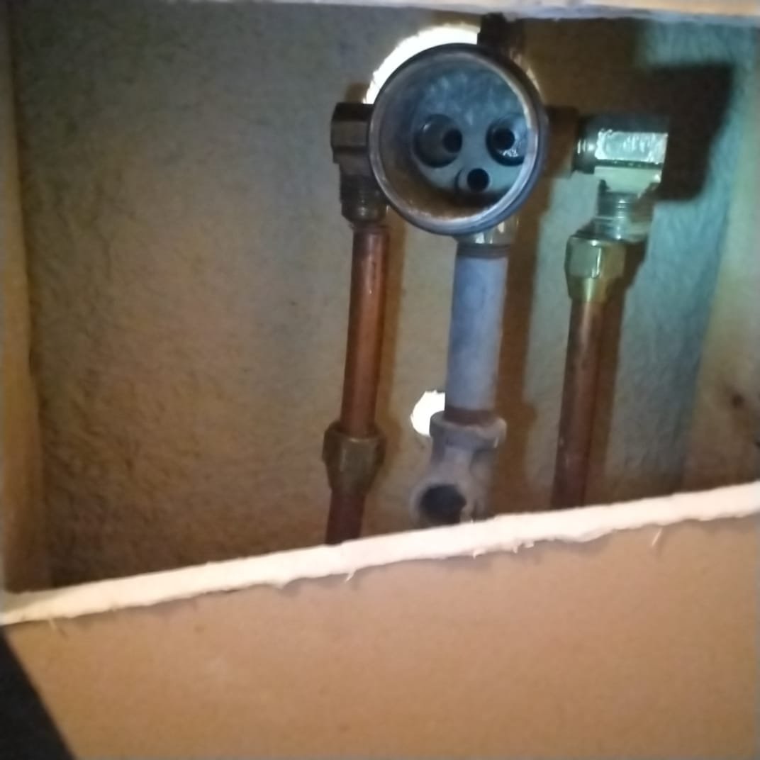 Section of newly accessed plumbing within a wall, showing several copper pipes connected to a central fixture.
