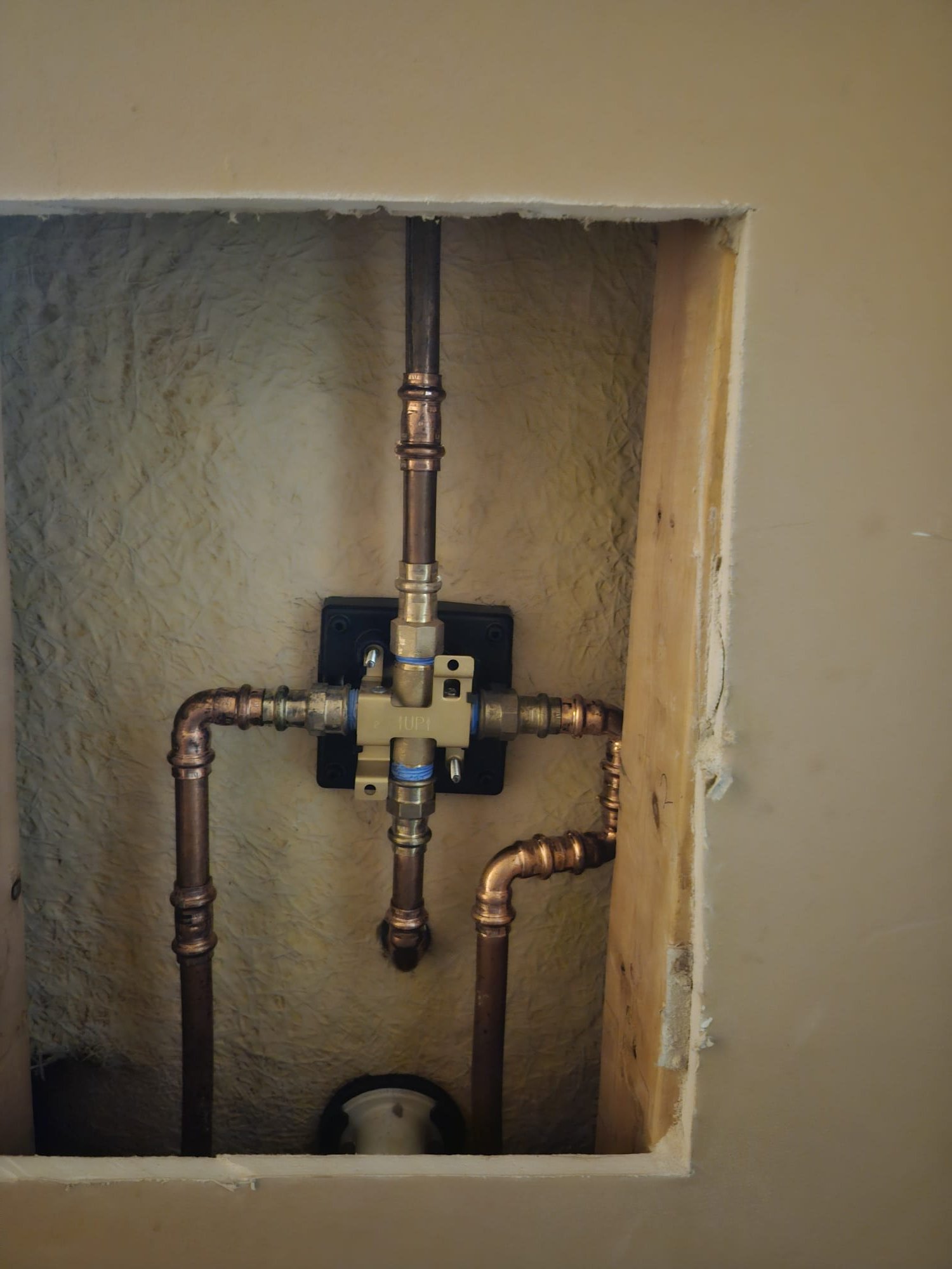 Neatly installed copper pipes and fittings inside a wall, demonstrating professional workmanship and secure connections.