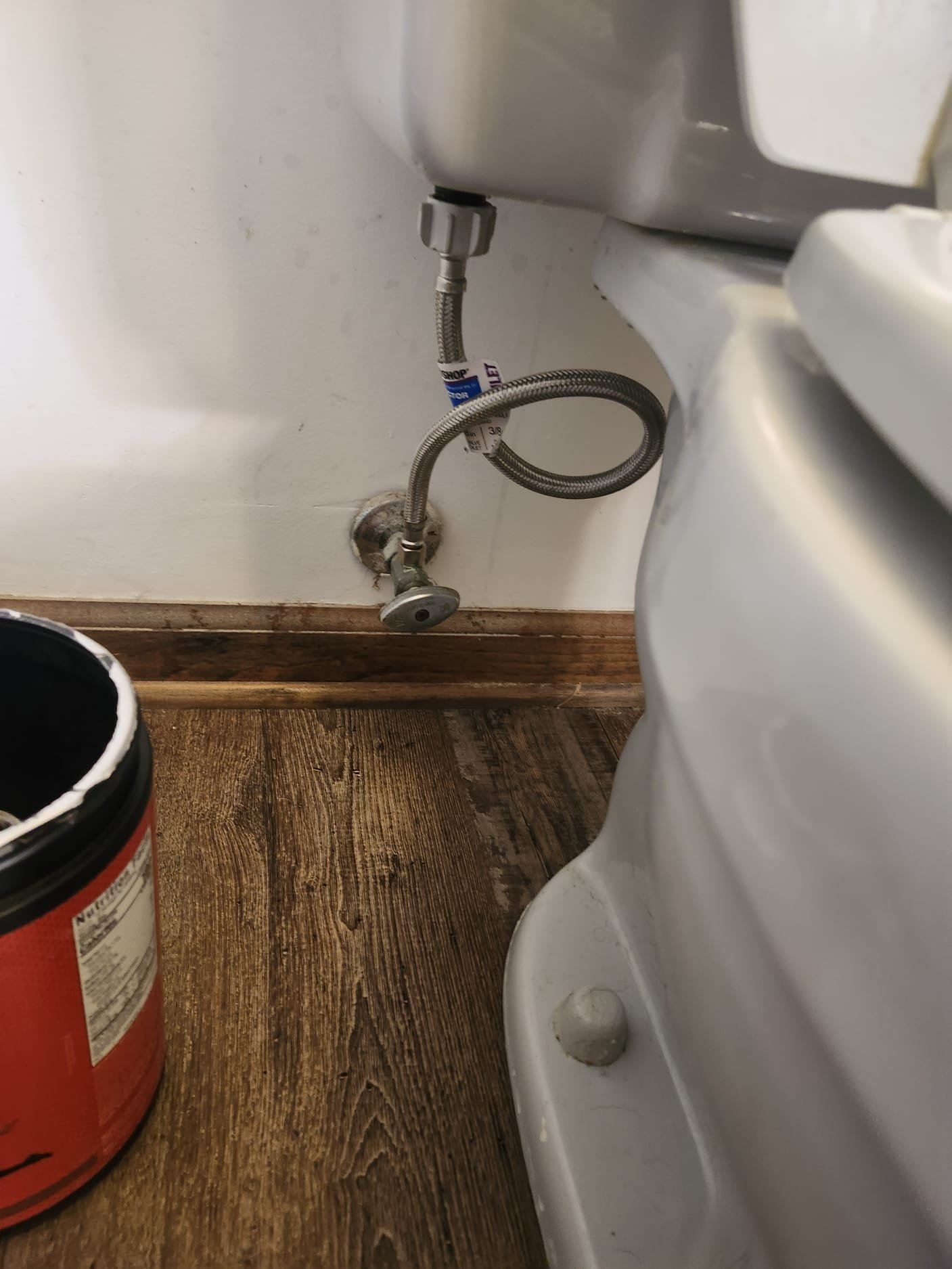 Image shows the plumbing connection behind a toilet, focusing on a clean, newly installed braided water supply line.
