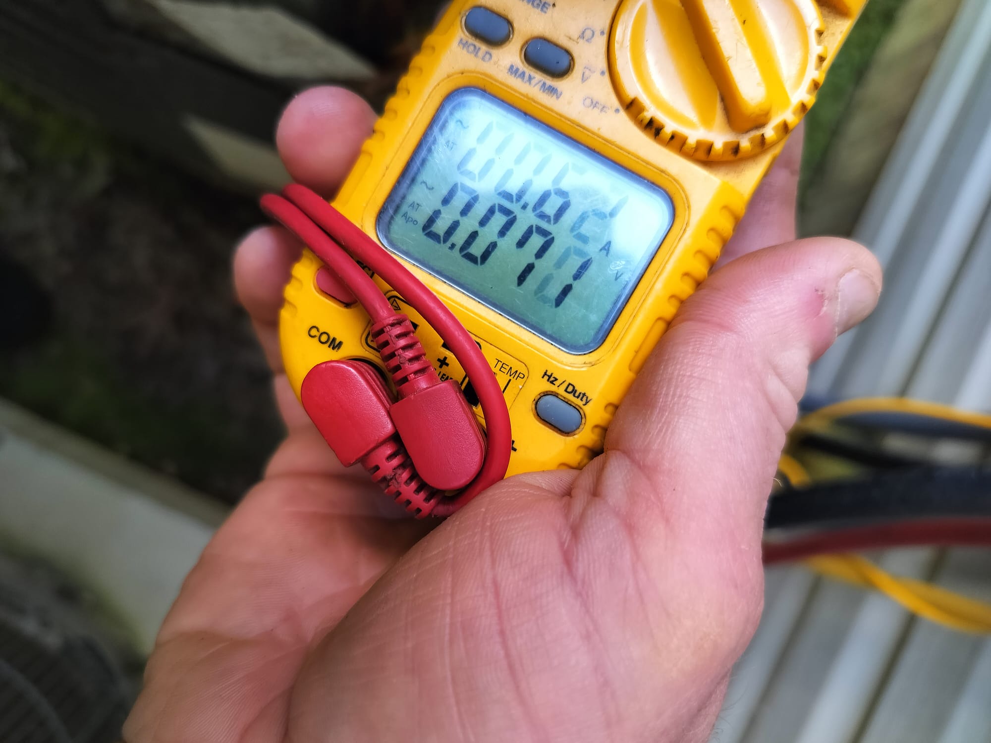 Technician holding a digital multimeter to measure electrical values during an HVAC inspection