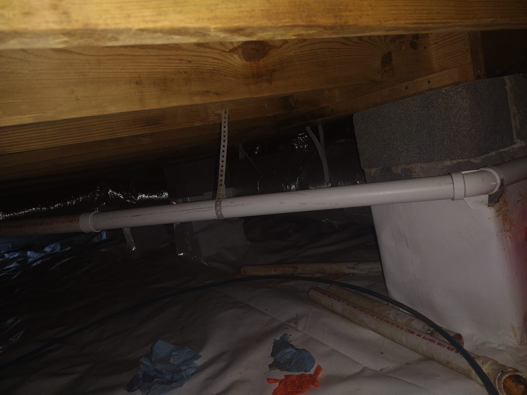 New, securely fastened PVC drain line installed under a kitchen floor