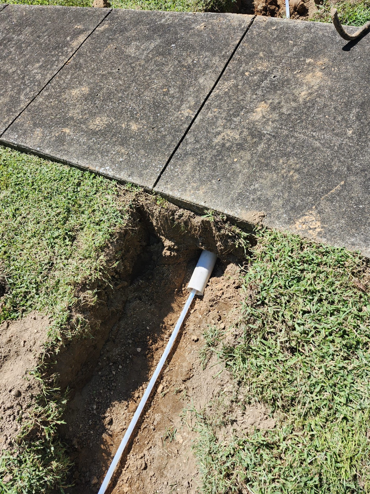 Trench with new white PVC pipe under concrete sidewalk