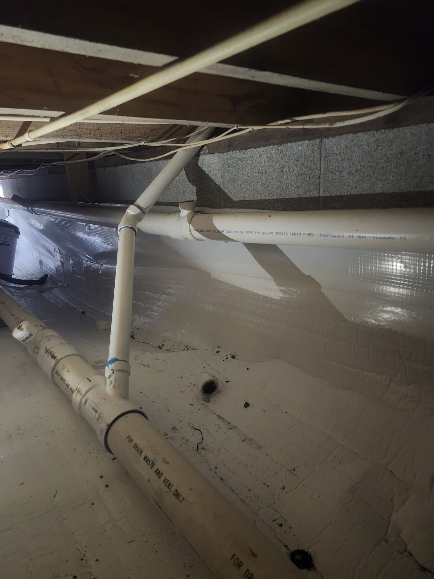 A clean, newly laid section of PVC drain lines in a basement crawl space