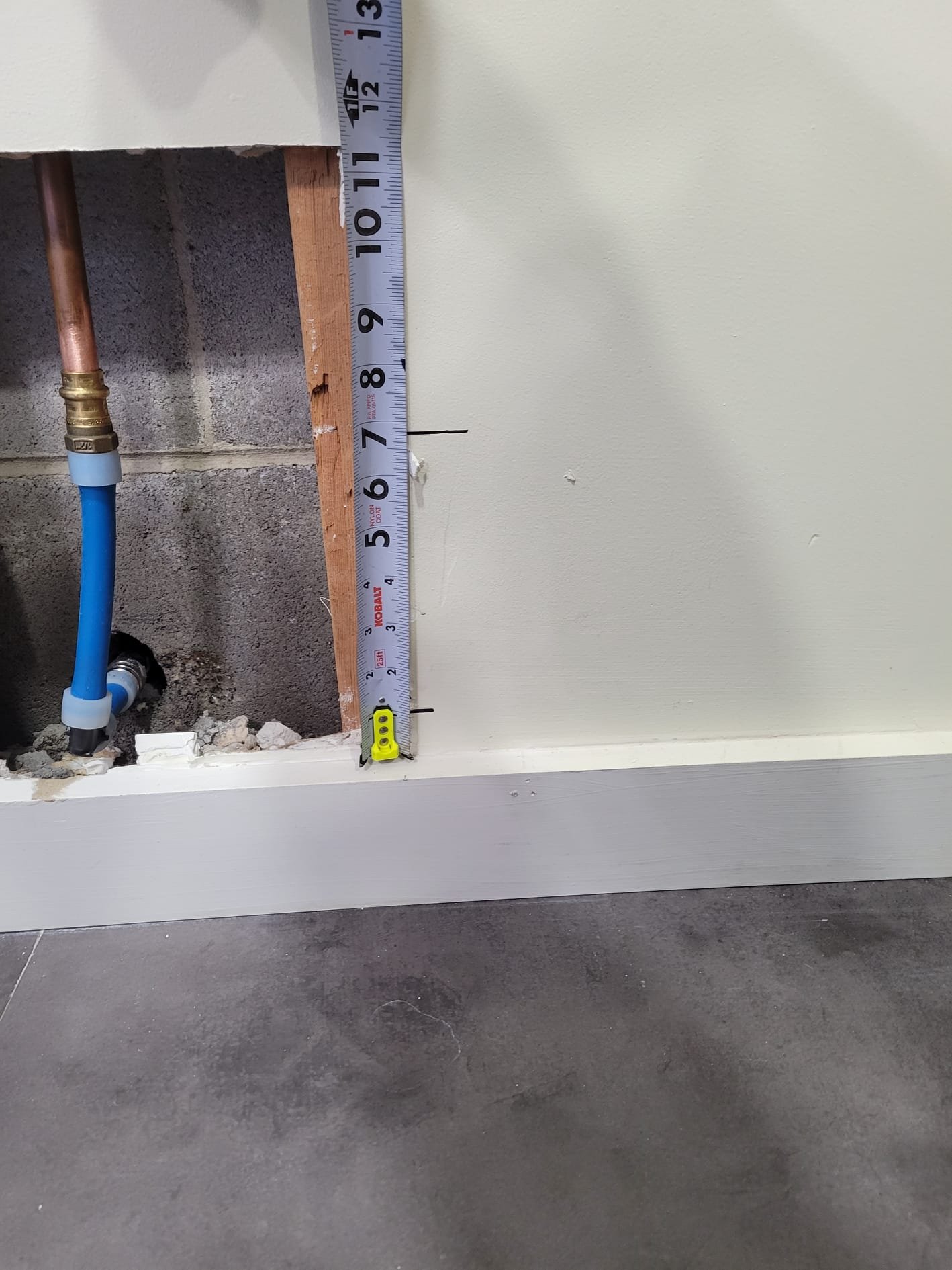 Exposed copper and PEX piping behind drywall, with tools measuring depth