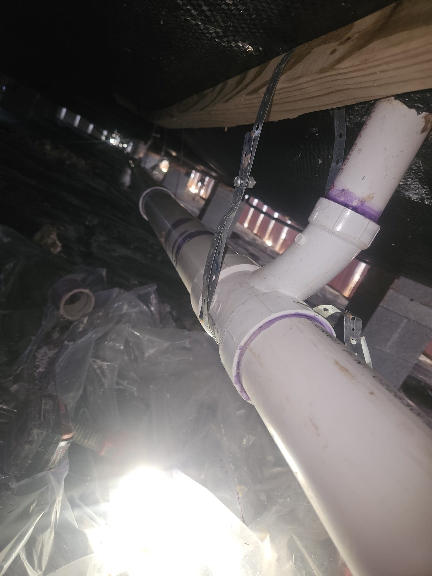 White PVC pipes securely fastened to floor joists in a crawl space.