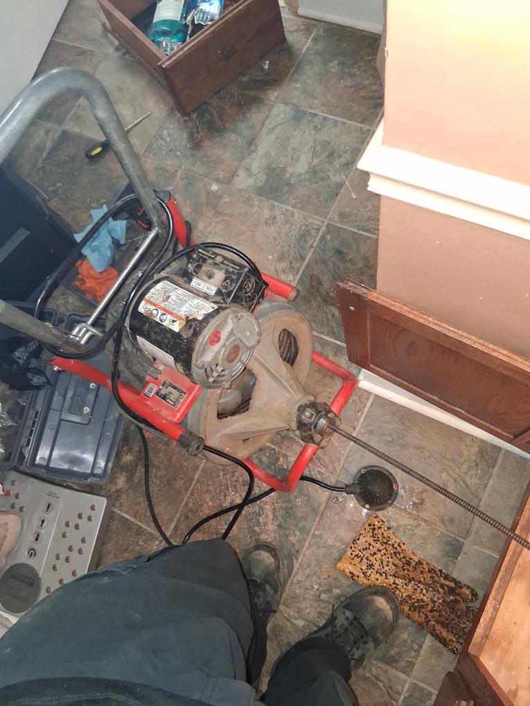 HEP technician using a drain auger under a sink