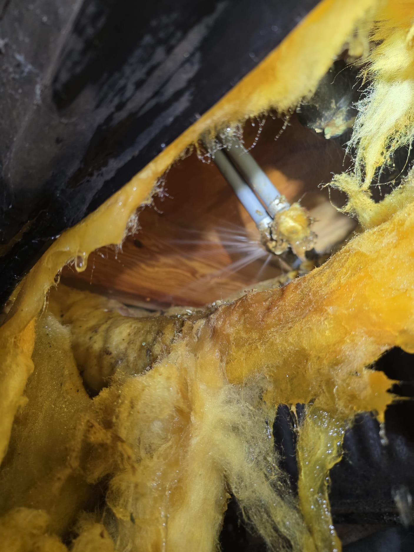 Close-up of a corroded pipe joint spraying water inside wet insulation