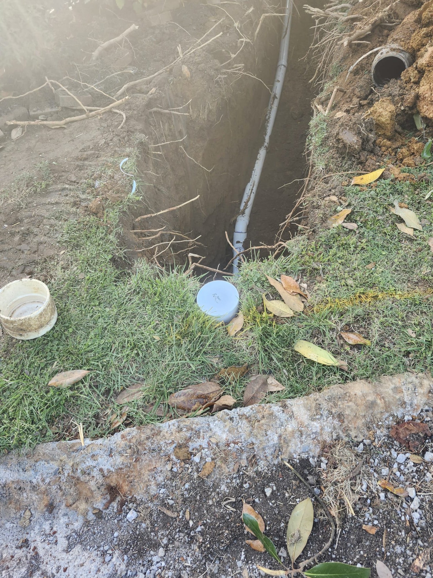 Fresh trench showing a cleanout riser and new PVC pipe before backfill