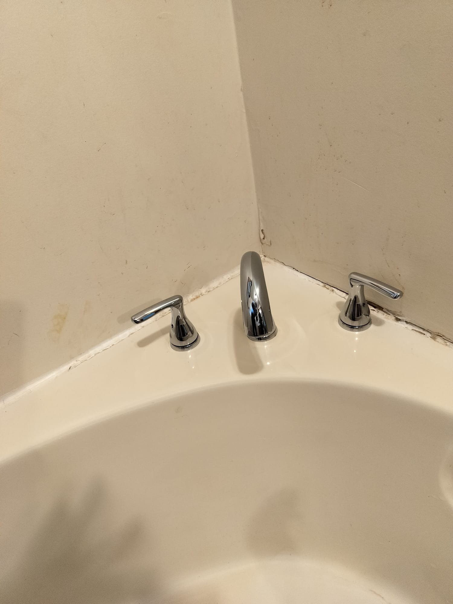 A corner bathtub with newly installed chrome plumbing fixtures