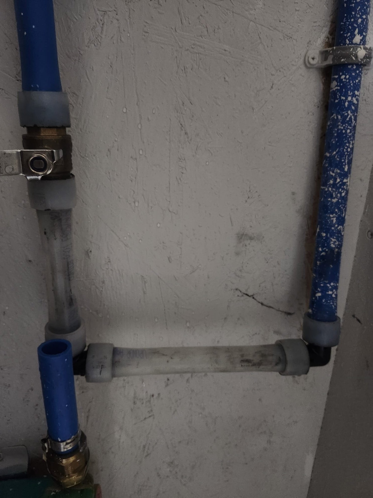 Blue PEX piping secured with fittings along a basement wall