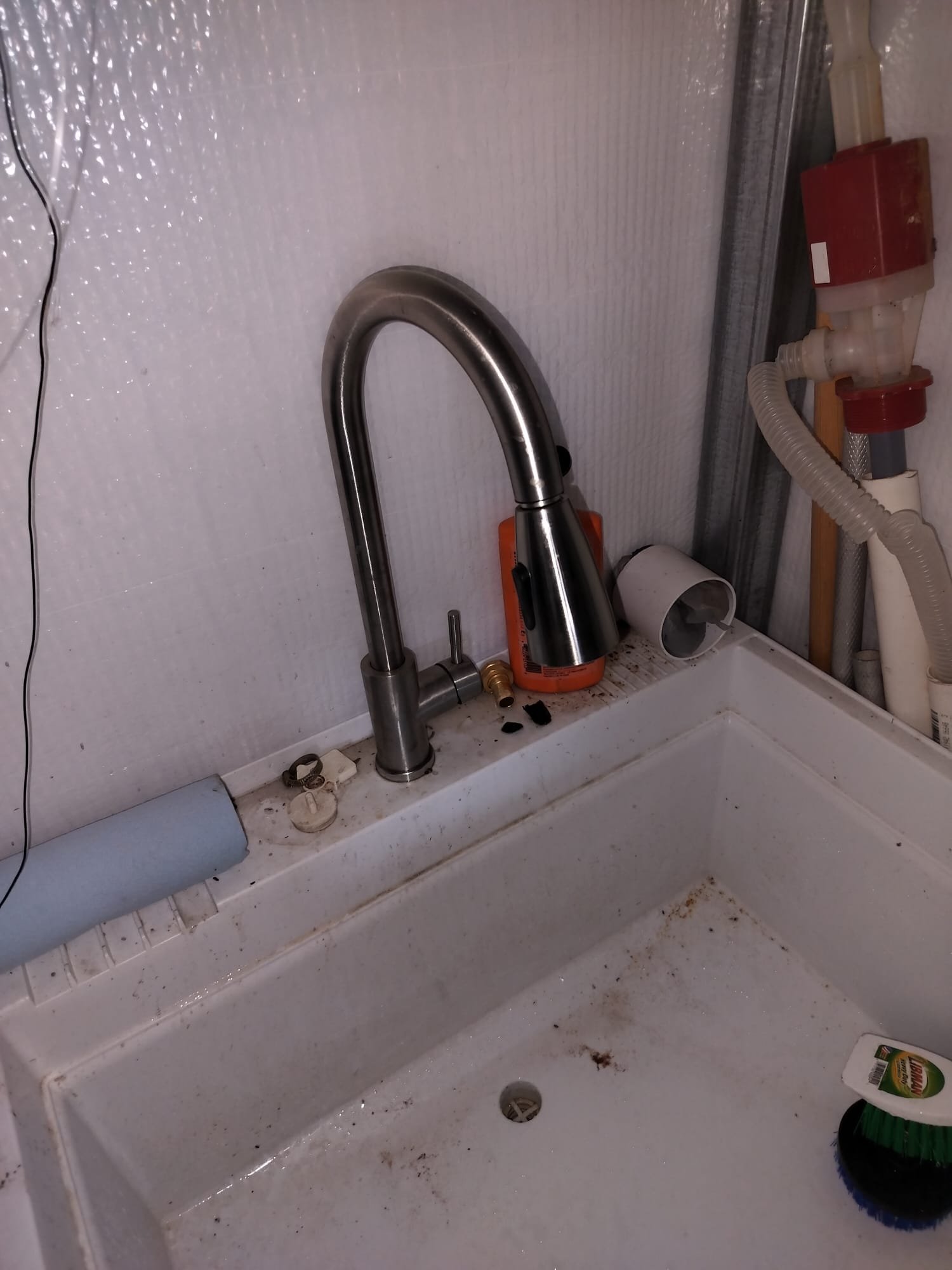 A utility sink area with exposed fittings and parts during a plumbing service call.