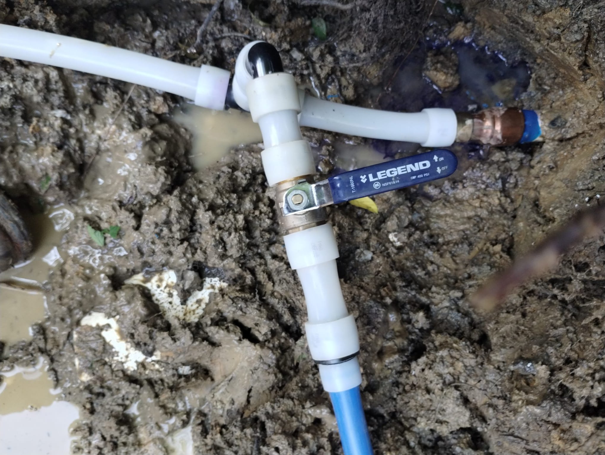 A repaired water line with a new shutoff valve and fresh fittings inside the trench